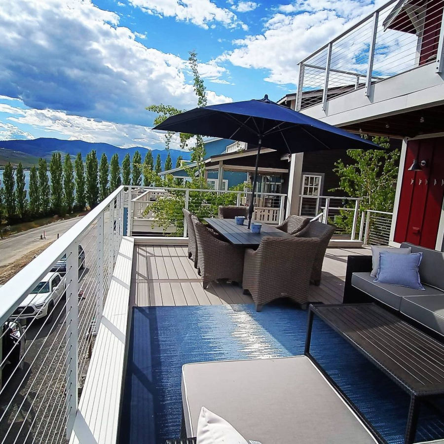 Balcony deck white cable railing overlooking lake water and green hedges.